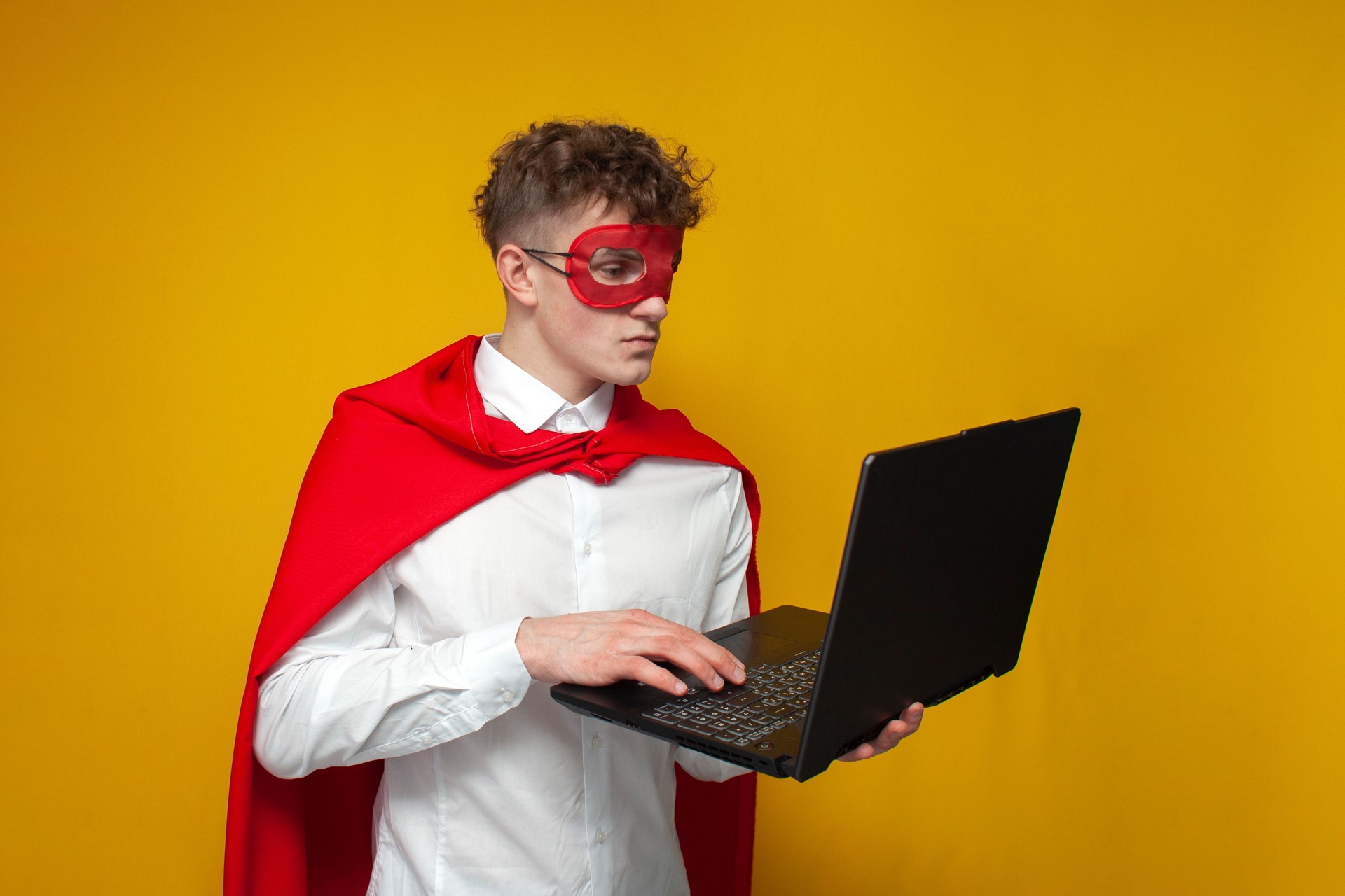 guy in a superhero costume uses a laptop on a yellow background, an employee superman types on a computer